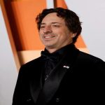 مردیبا ست رسمی کت شلوار مشکی لبخندی بر صورت دارد و در یک مصاحبه حاضر شده است