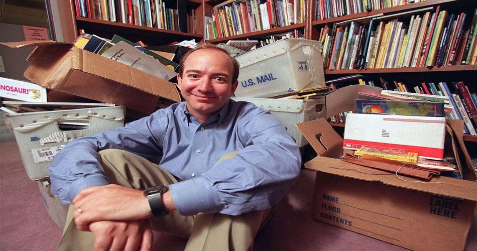 یک فرد در حال نشستن روی زمین در اتاقی پر از کتاب‌ها و جعبه‌های مقوایی، پشت سر او قفسه‌های پر از کتاب قرار دارد. فضای اتاق حالت قدیمی و ابتدایی دارد. نور نرم و طبیعی داخل اتاق پخش شده است.