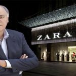 آمانسیو اورتگا با ست رسمی با کت شلوار و در پشتش تصویری مغازه ایی از zara