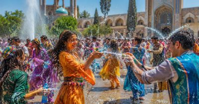 جمعی از جوانان با لباس‌های رنگارنگ در حیاطی با معماری سنتی ایرانی زیر نور آفتاب به هم آب می‌پاشند؛ دختری با لباس نارنجی در حال خندیدن و مردی روبه‌رویش آب می‌پاشد، قطرات آب در هوا پخش شده‌اند